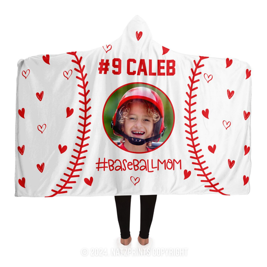 A white hooded blanket featuring red stitching designed to look like a baseball, with small red hearts scattered throughout